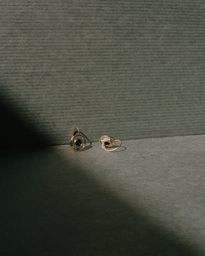 Two gold Rebecca Mapes earrings on a textured green surface