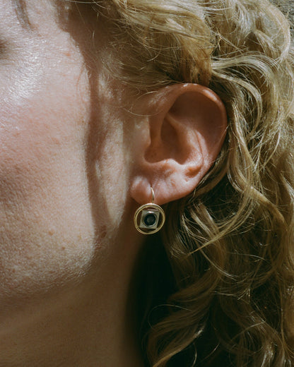 Close-up of an ear wearing a gold Rebecca Mapes earring with a blue gemstone.