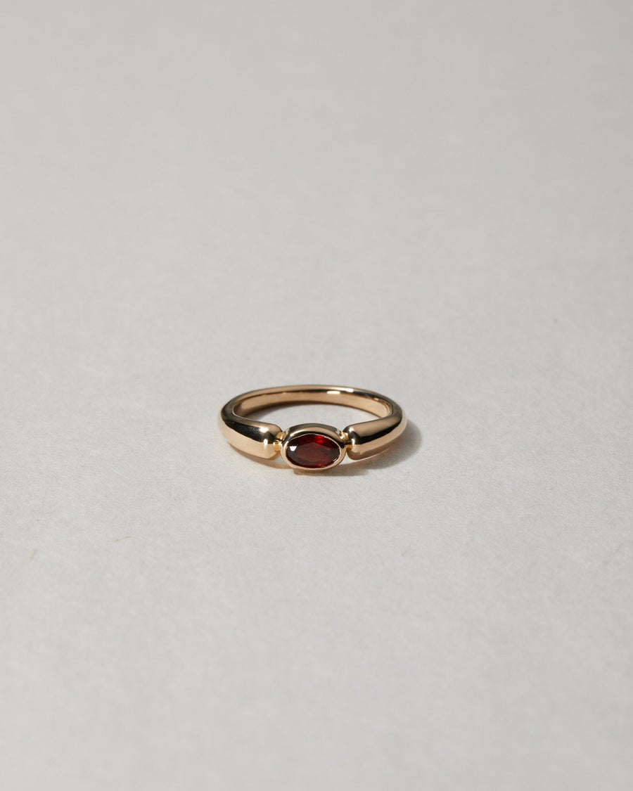A gold ring with a red garnet or sapphire stone, positioned against a neutral background.